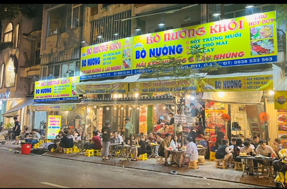 The facade at night — yellow sign, sidewalk tables
