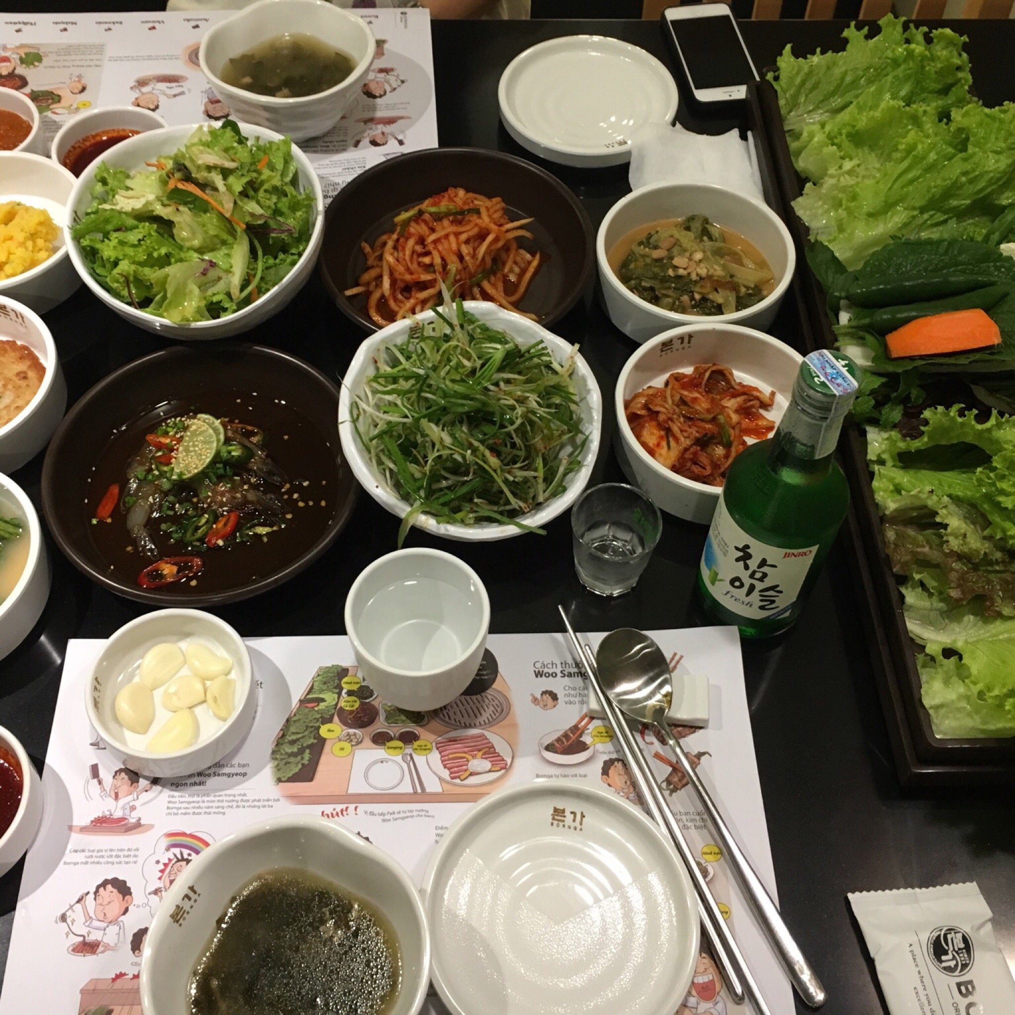 반찬, 쌈 채소, 소주로 가득한 한국식 구이 테이블