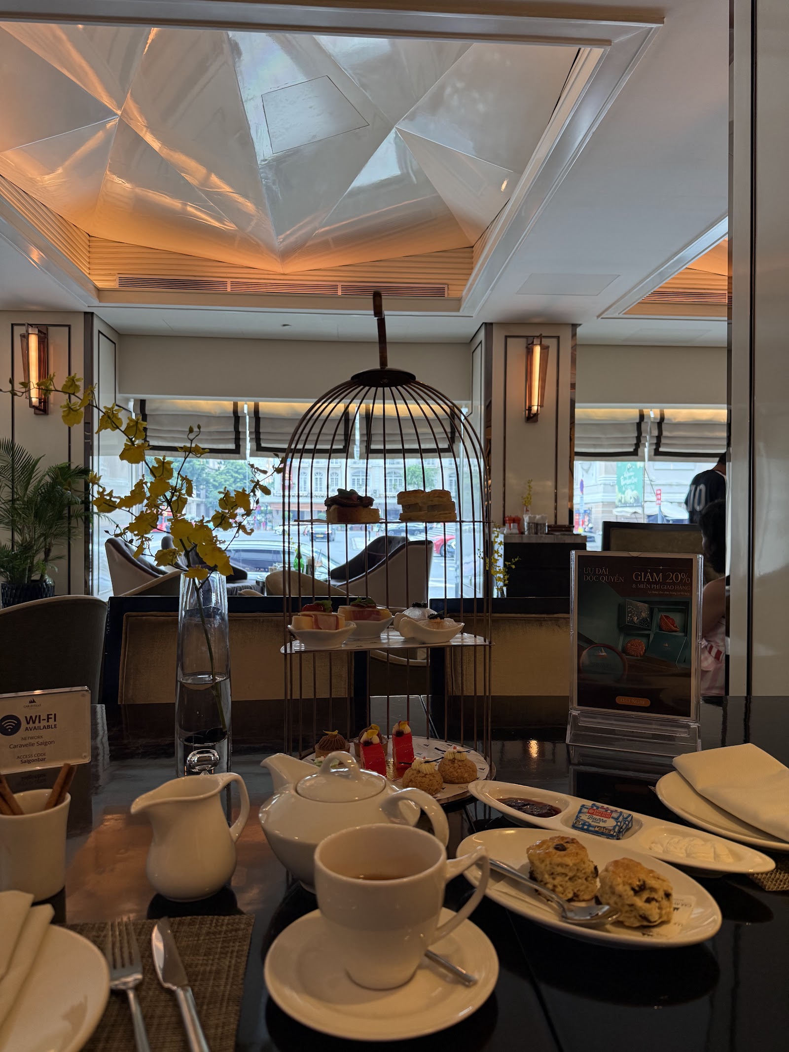 Trà chiều trên giá lồng chim: ấm trà trắng, tách trà, bánh scone kèm mứt dâu, bánh ngọt nhiều tầng