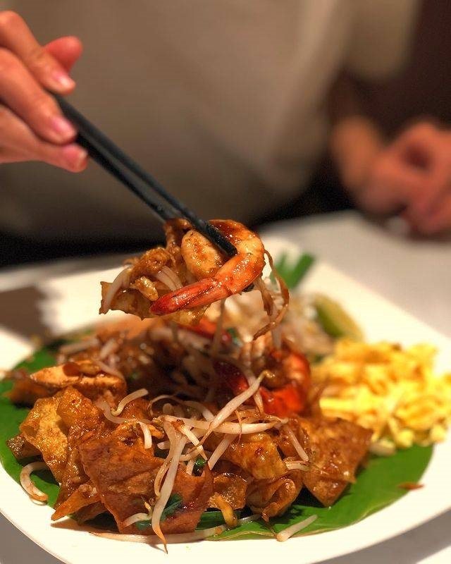Pad Thai with shrimp, lifted on chopsticks over a banana leaf
