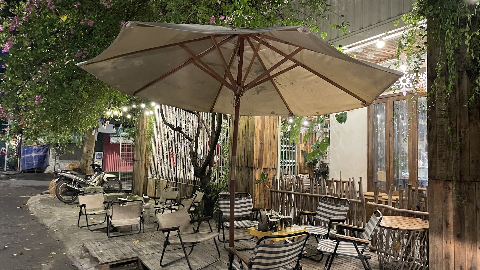 CƯ XÁ's night patio — canvas umbrella, camping chairs, string lights