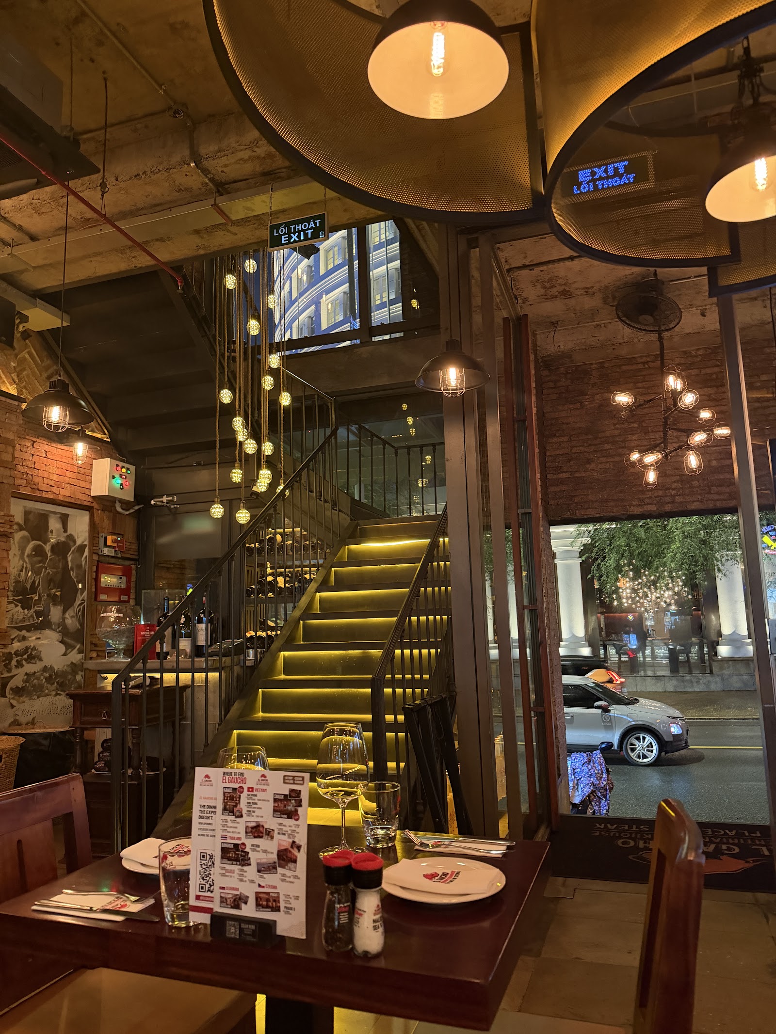 The dining room with its lit staircase, brick walls and bulb strings