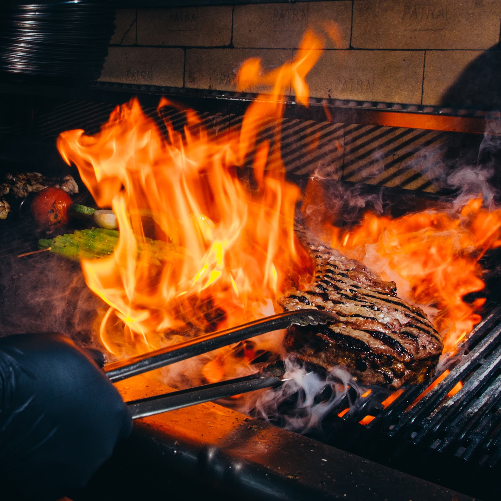 The steak on the open-flame grill, tongs turning it