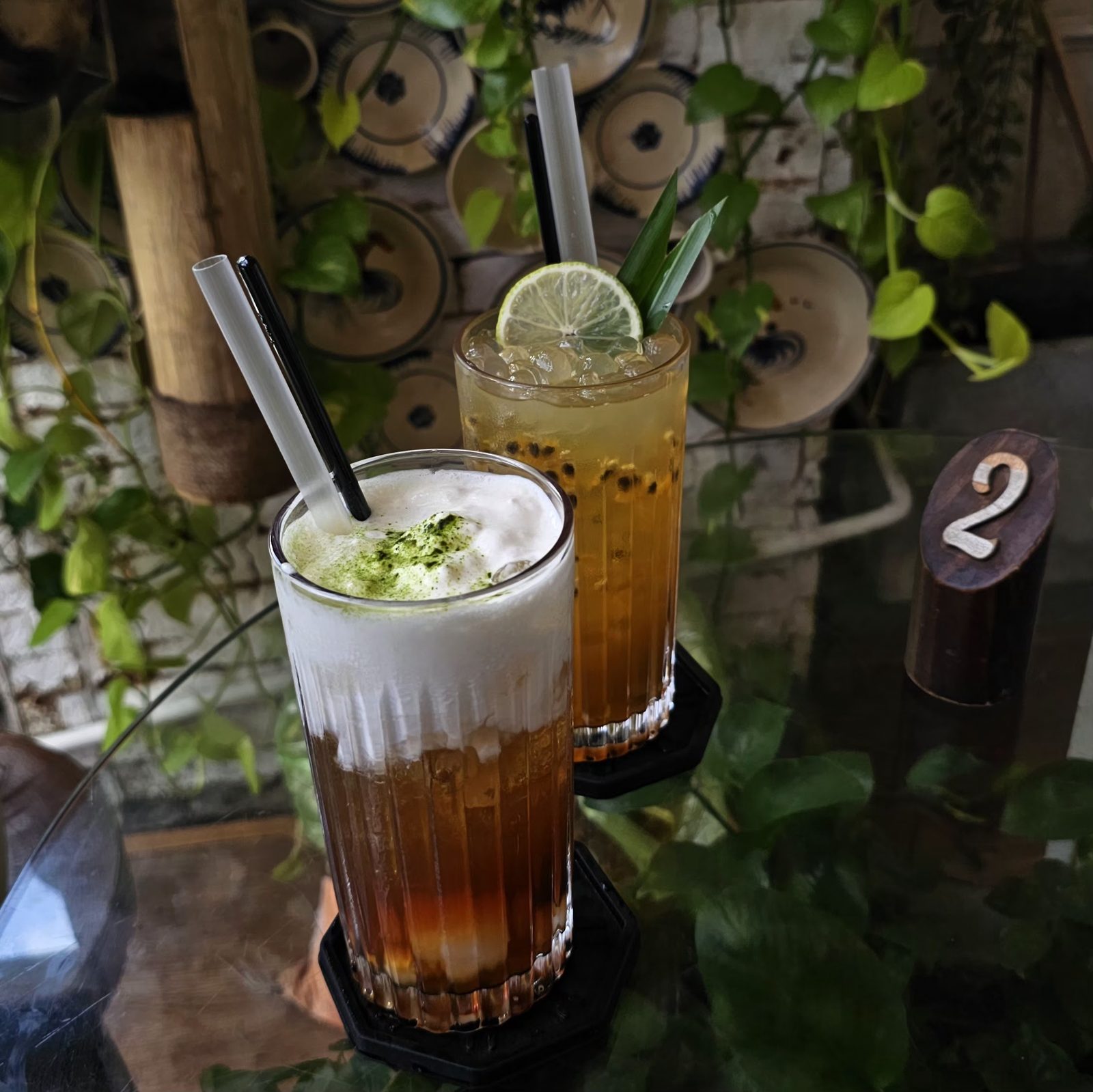 Good Days Tea & Coffee — hai ly phân tầng trên bàn kính, tường đĩa gốm, cây leo, thẻ số bàn gỗ