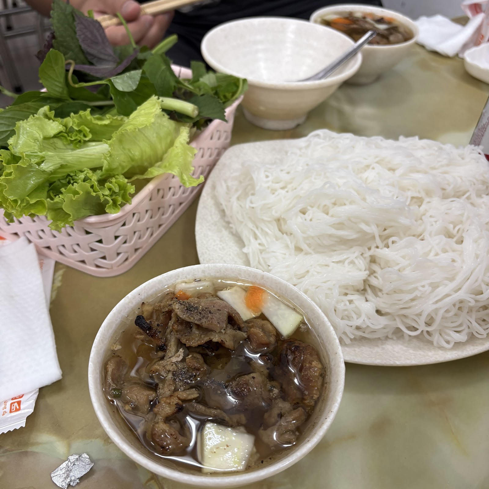Closeup of the bún chả — grilled pork and patties in the dipping bowl with carrot and daikon pickles