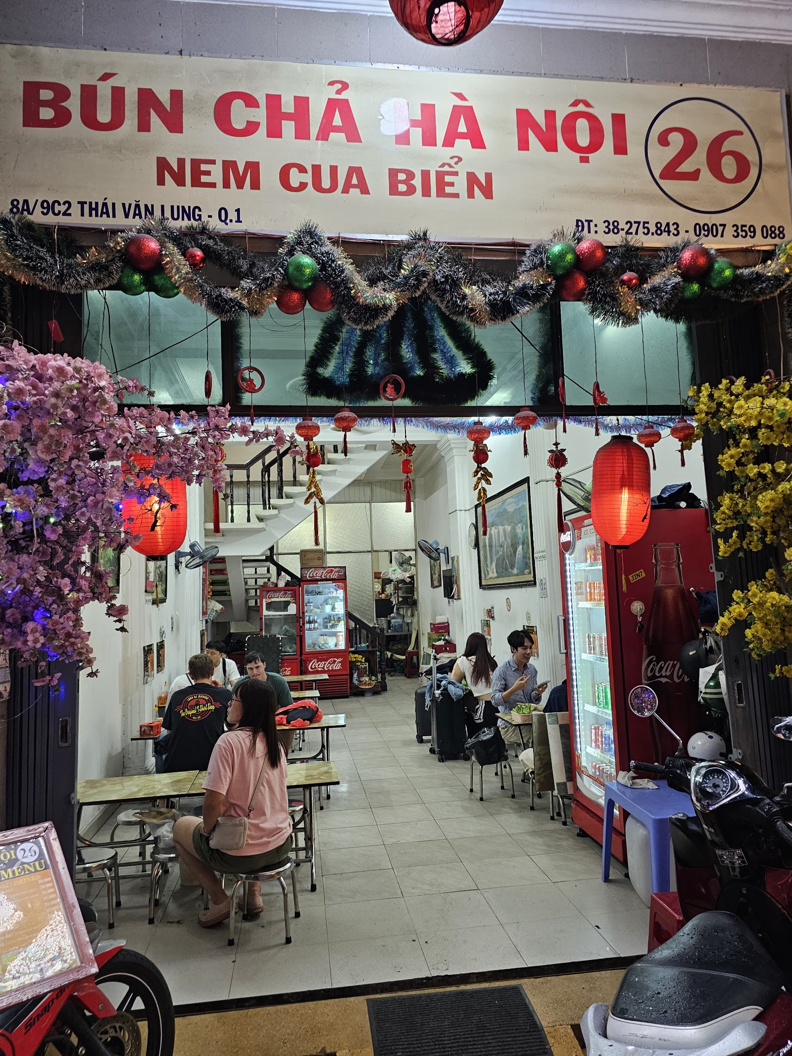 The evening storefront — the red-lettered BÚN CHẢ HÀ NỘI 26 sign, red lanterns and the peach tree