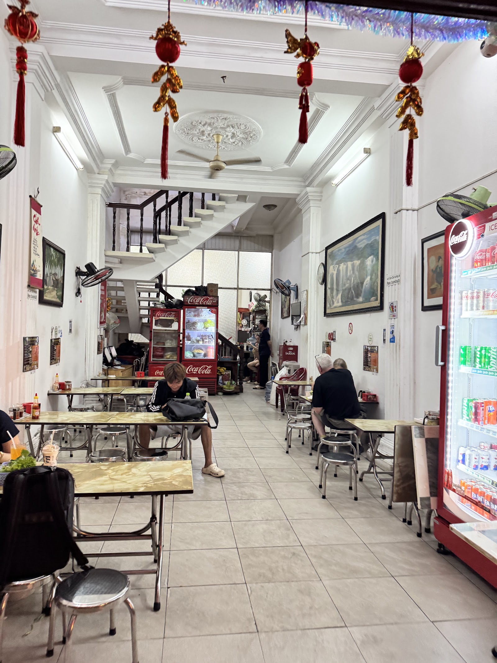 The dining hall — white walls, patterned plaster ceiling, red lanterns hung high, the white staircase, stainless tables