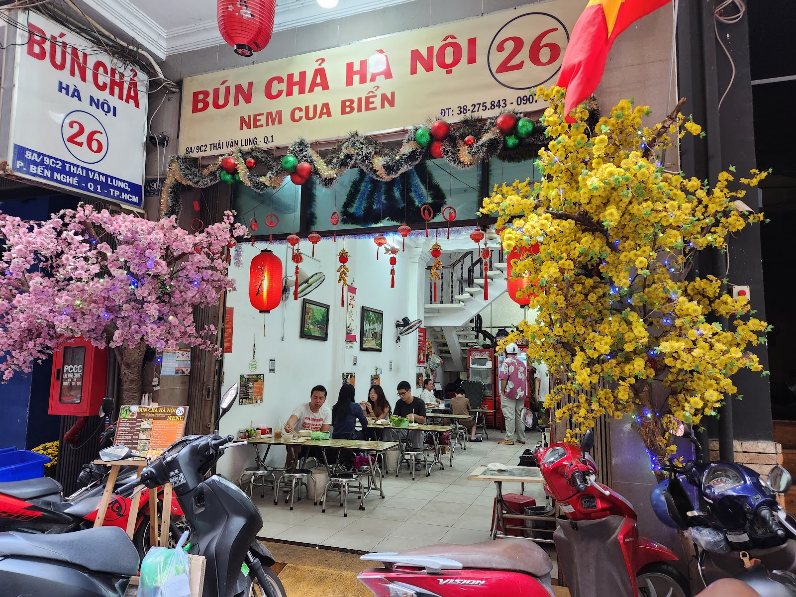 The daytime storefront — diners at tables between the pink peach tree and the yellow apricot tree