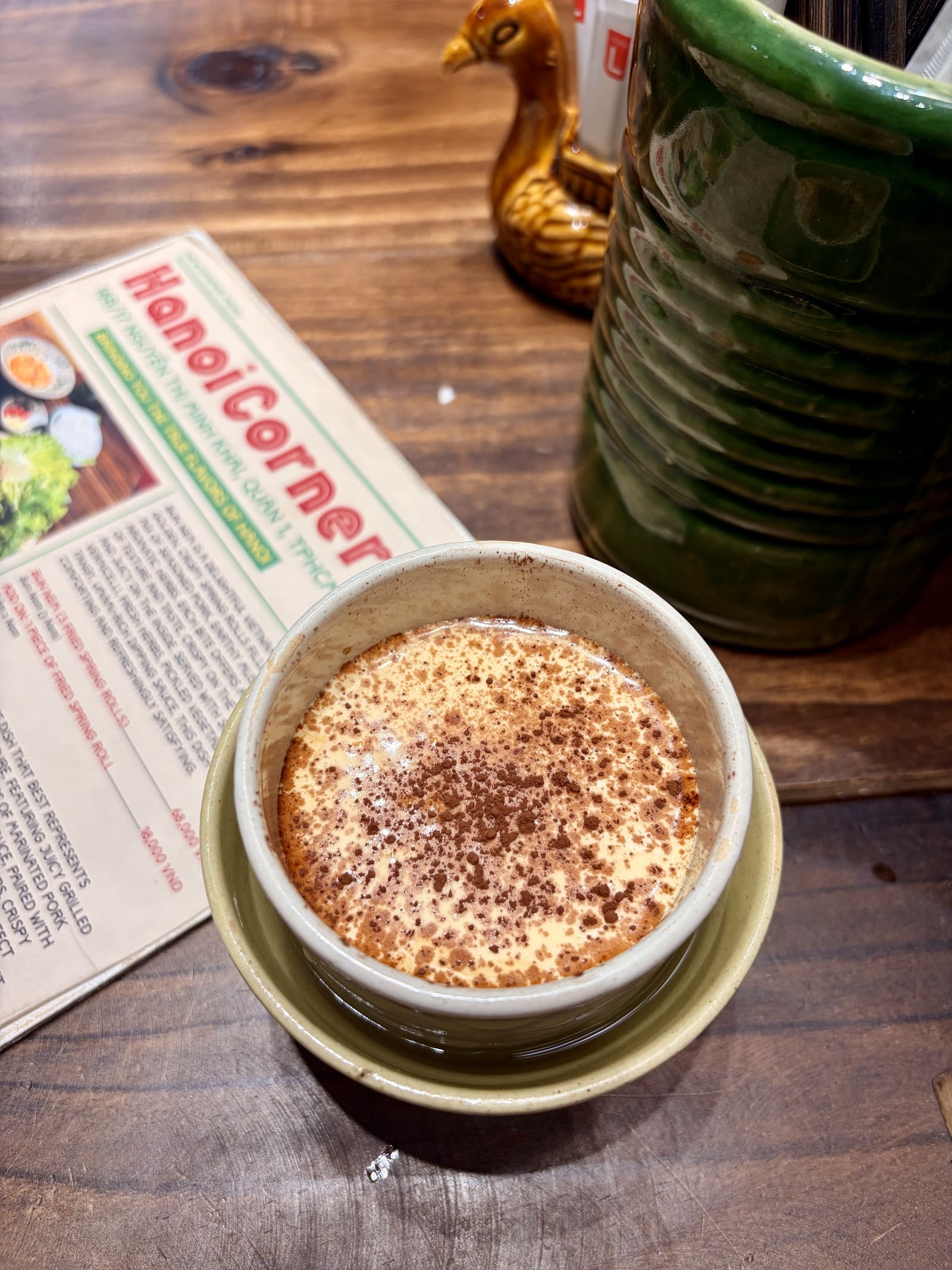 Ly cà phê trứng rắc cacao cạnh cuốn sổ tay Hanoi Corner