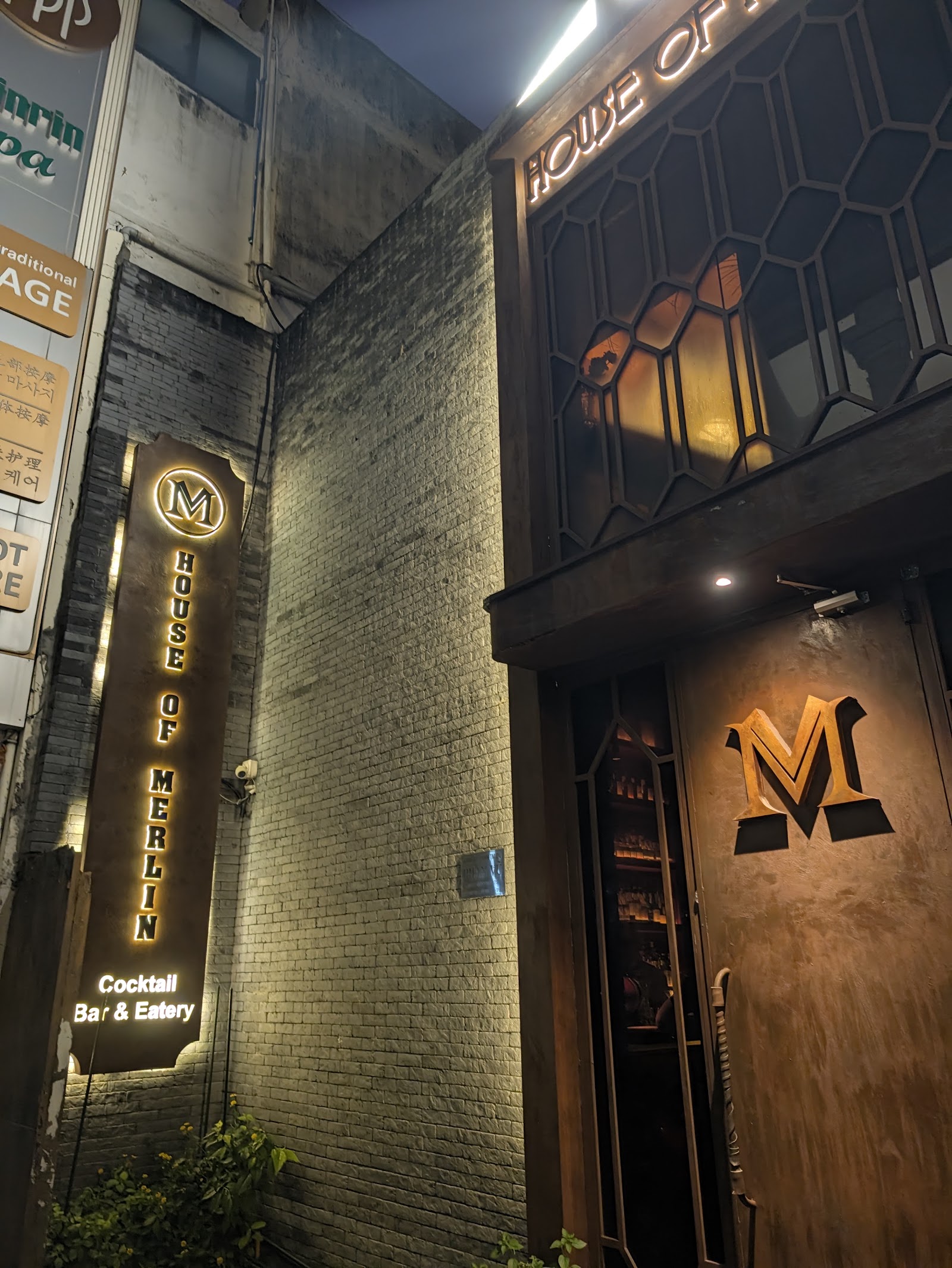 Mặt tiền về đêm — biển hiệu House of Merlin phát sáng
