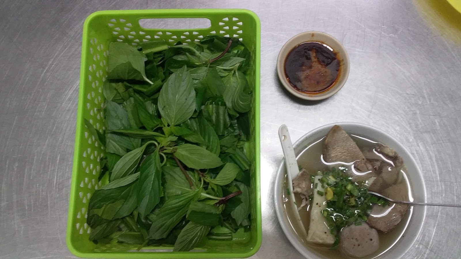 Rổ rau xanh và chén nước chấm trên bàn inox — ảnh của khách