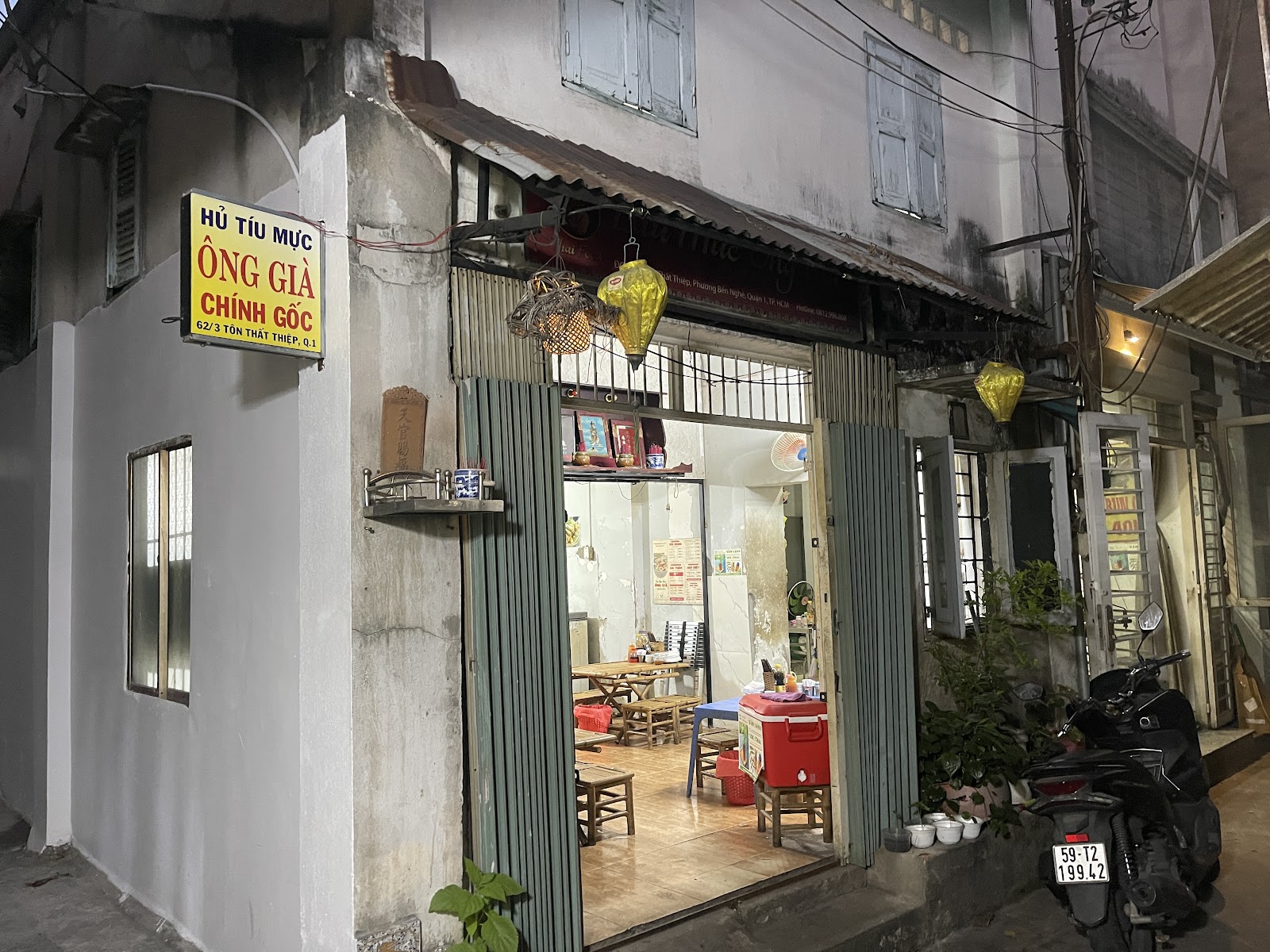 The lit doorway at night — yellow lanterns and the glowing sign in the alley