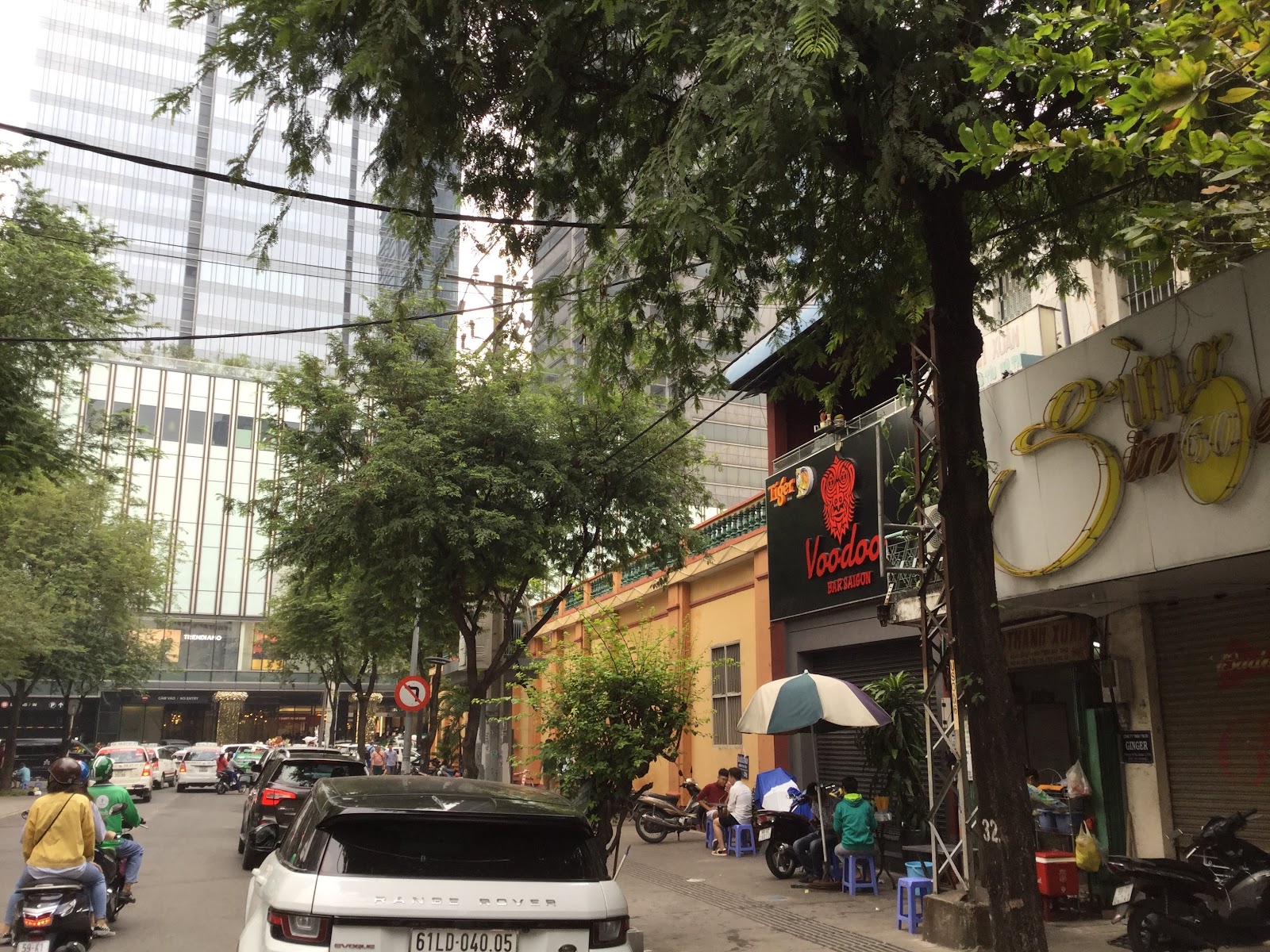 Đường Tôn Thất Thiệp trước quán — hàng cây, tòa nhà, ghế nhựa xanh trước cửa