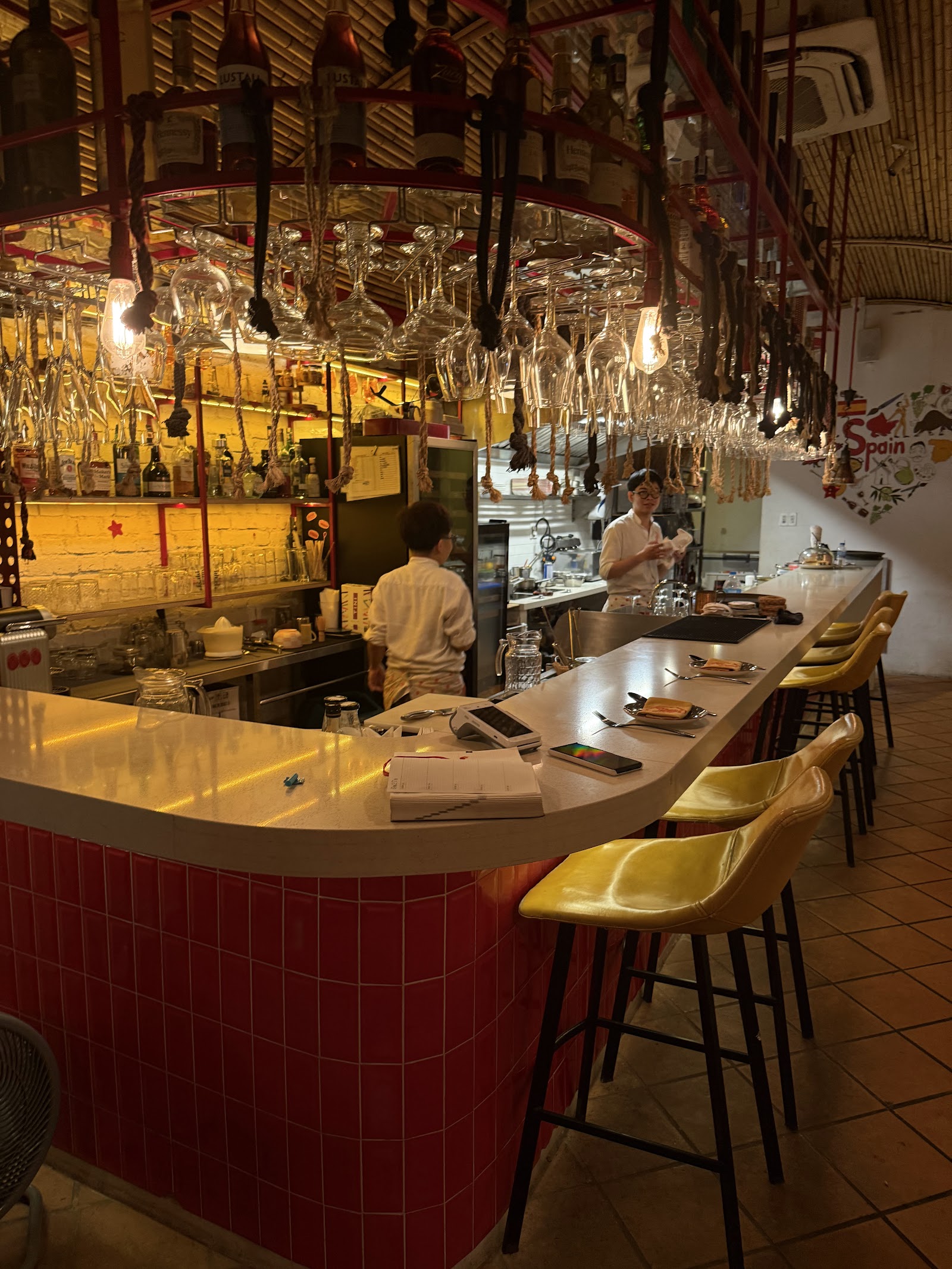 The red-tile bar with rows of hanging wine glasses and staff at work
