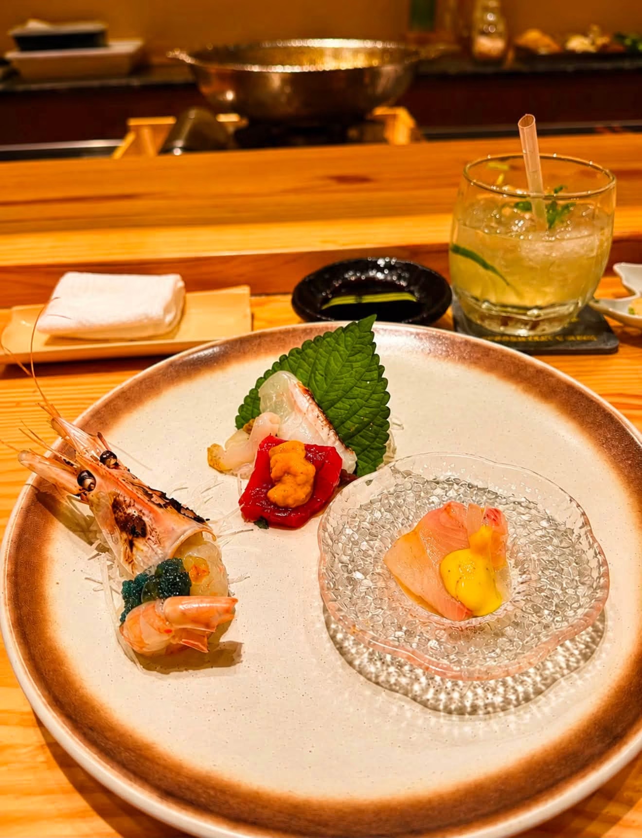 Sashimi platter: grilled shrimp head, uni, shiso on the wooden counter