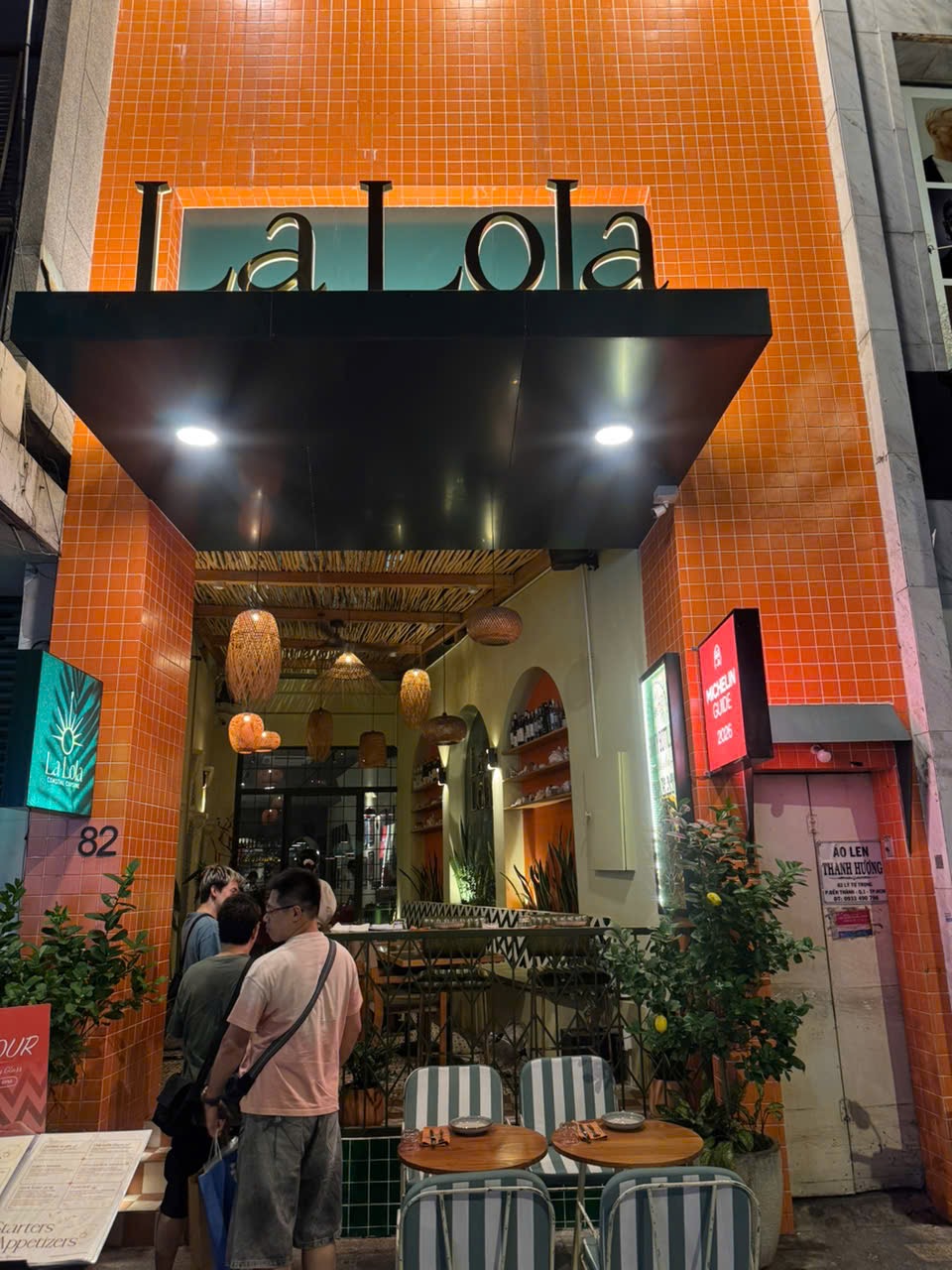 Mặt tiền La Lola về đêm với biển hiệu và bàn ghế ngoài trời
