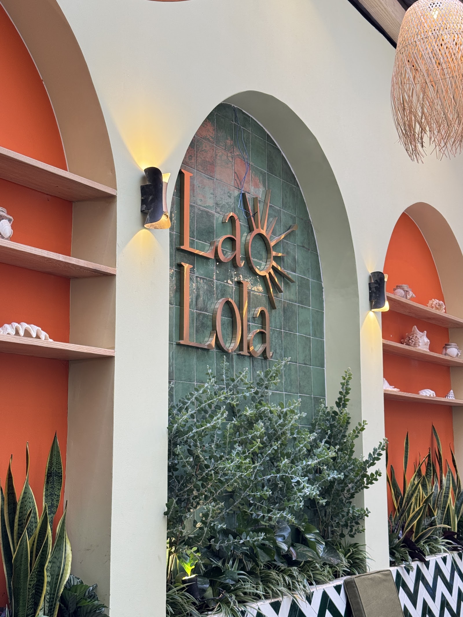 Tường logo La Lola với hốc vòm terracotta, đèn tường và đèn mây