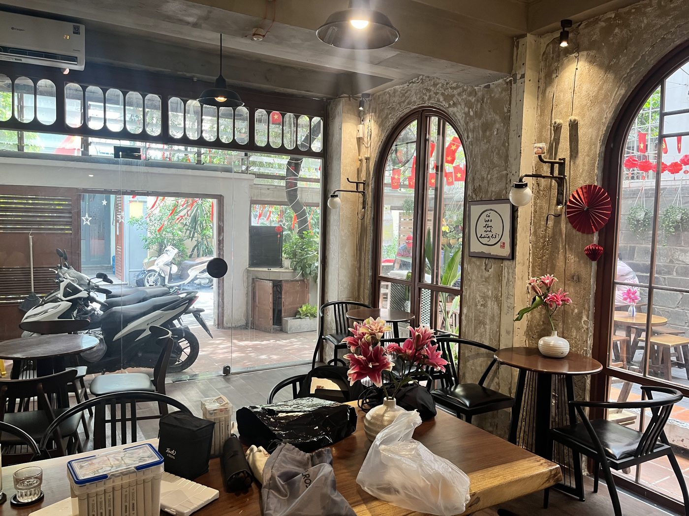Gian trong: tường bê tông thô, cửa kính vòm, bàn gỗ với bình hoa