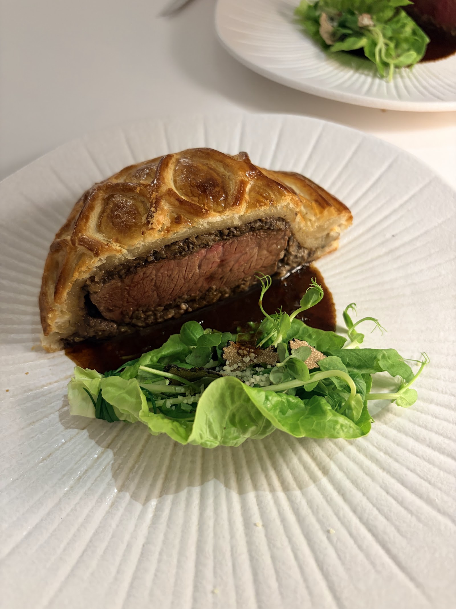 Sliced beef wellington — pink beef inside crisp puff pastry, with greens and sauce