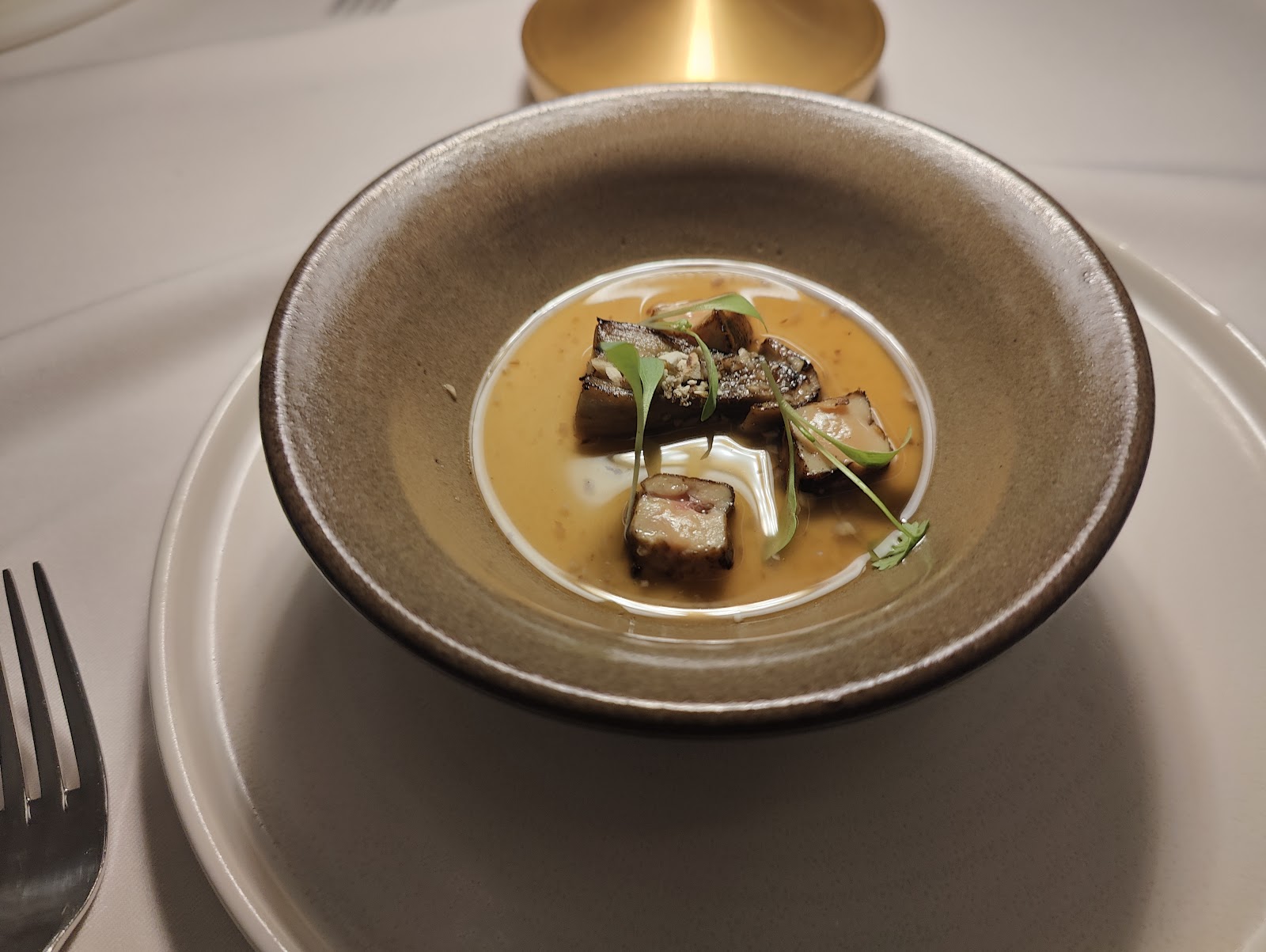 Cream of mushroom soup in a brown ceramic bowl with diced mushrooms and micro-greens