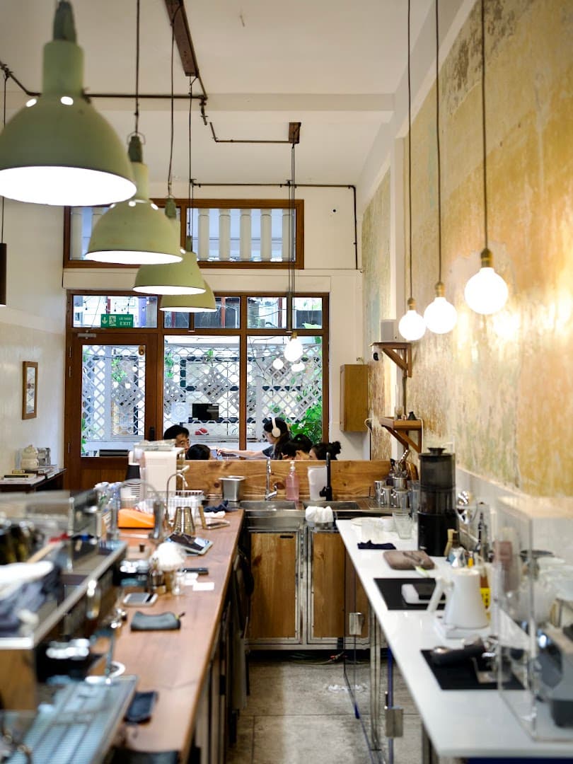 Manki — the long wooden bar counter, green enamel pendant shades, windows onto the trees