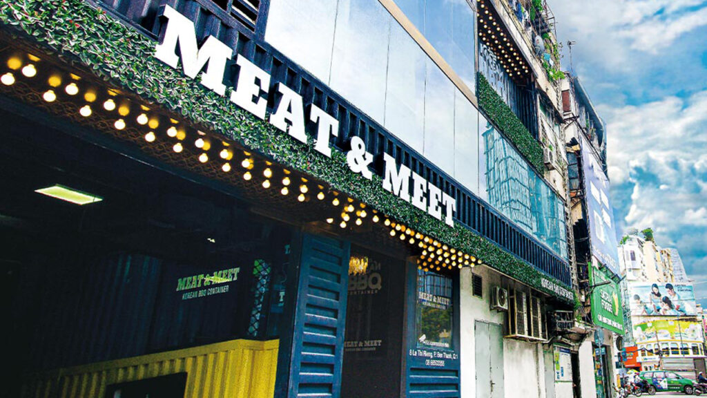 MEAT & MEET Lê Thị Riêng facade — container steel cladding, white letters, Edison-bulb strings