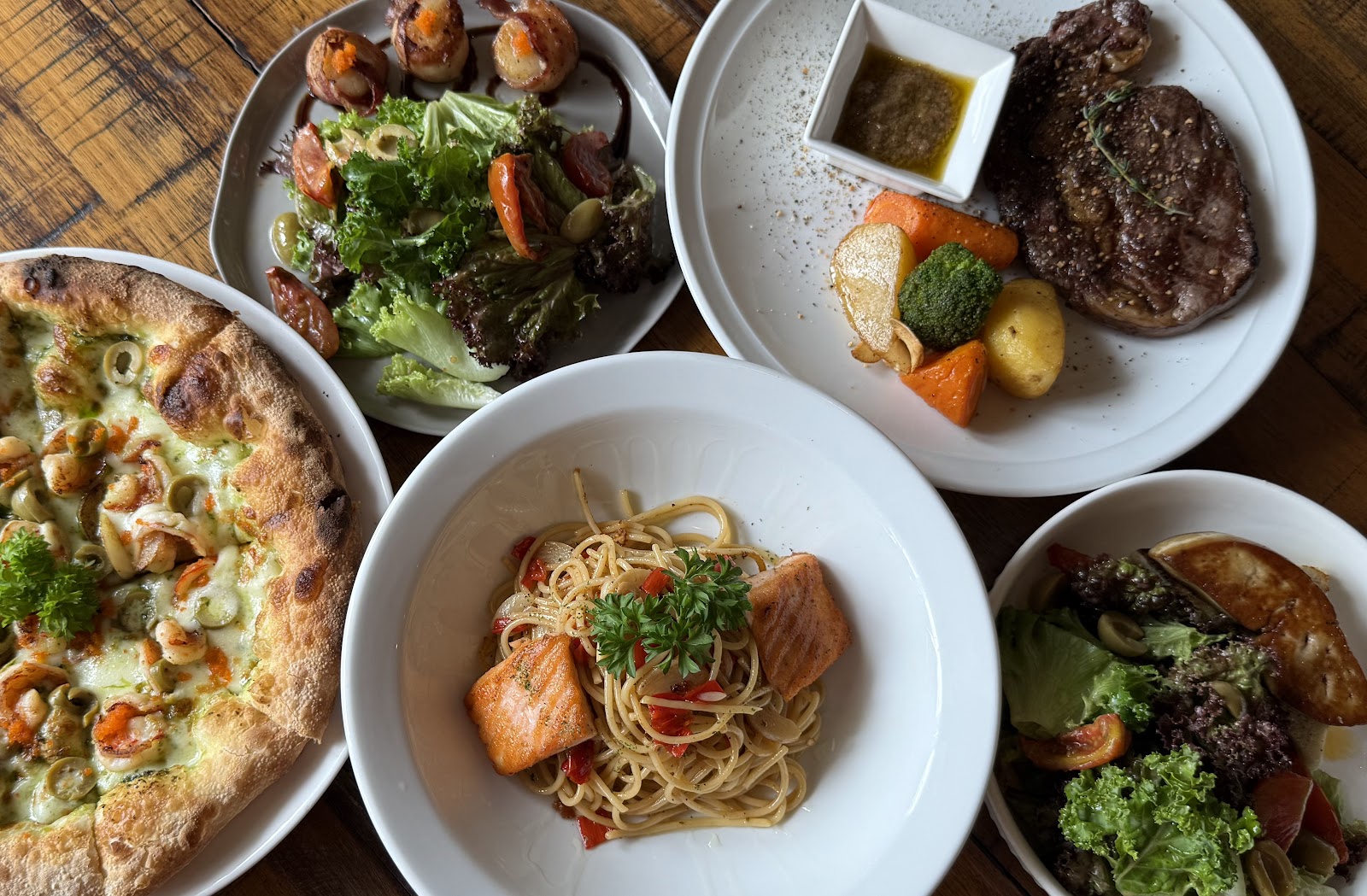 Overhead table spread — pizza, burrata salad, steak, salmon spaghetti