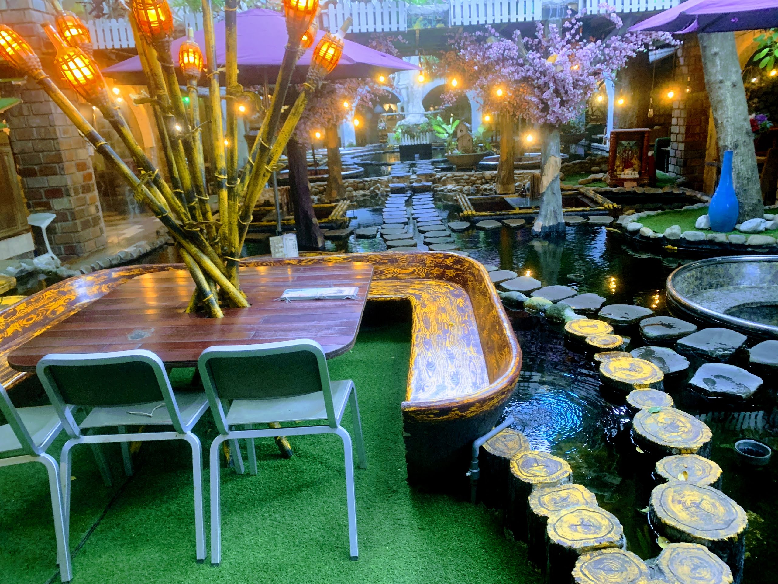 Oasis koi pond at night with bamboo torches and wooden boat tables