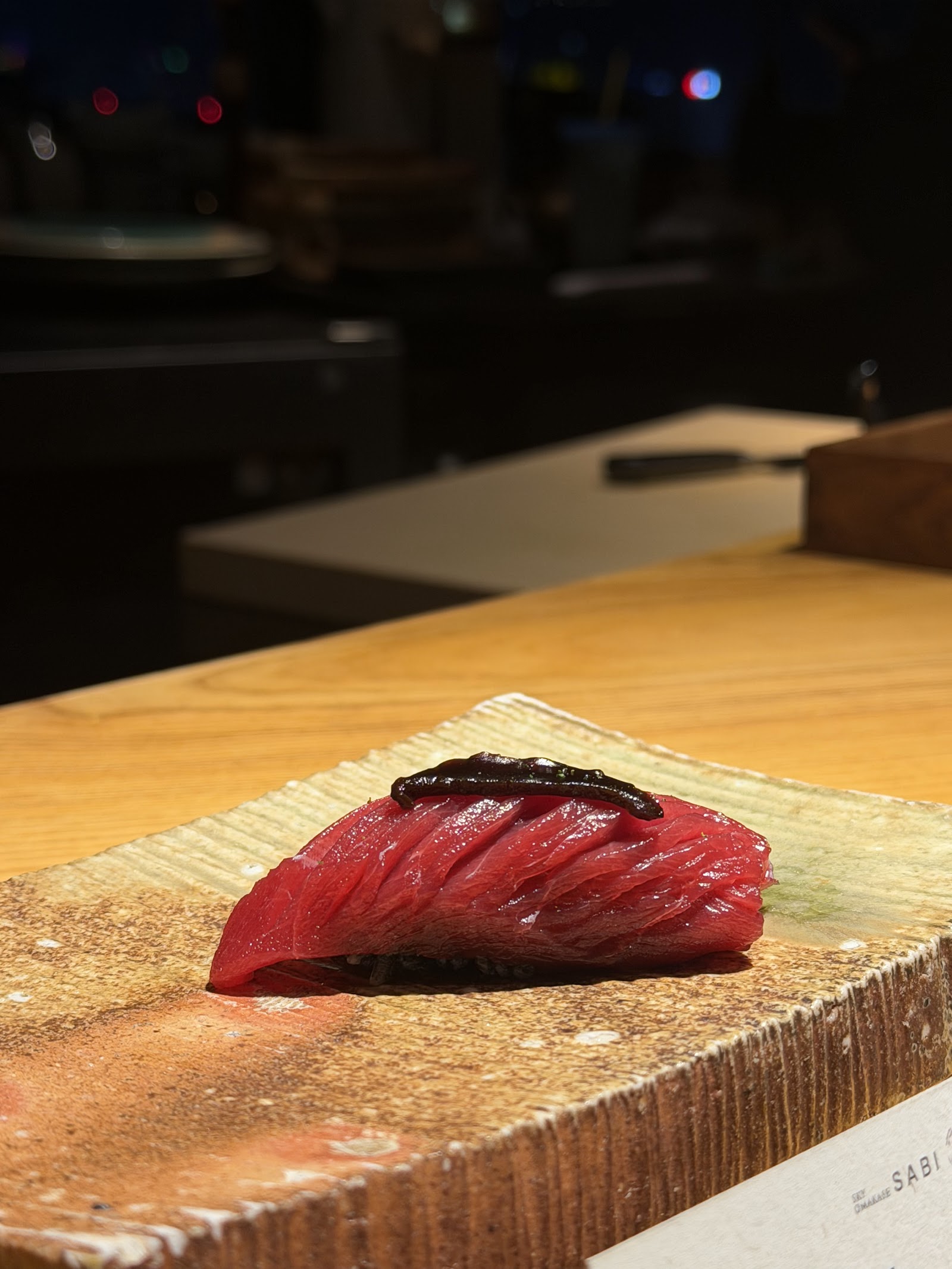 Nigiri cá ngừ ban đêm — ánh đèn thành phố sau quầy