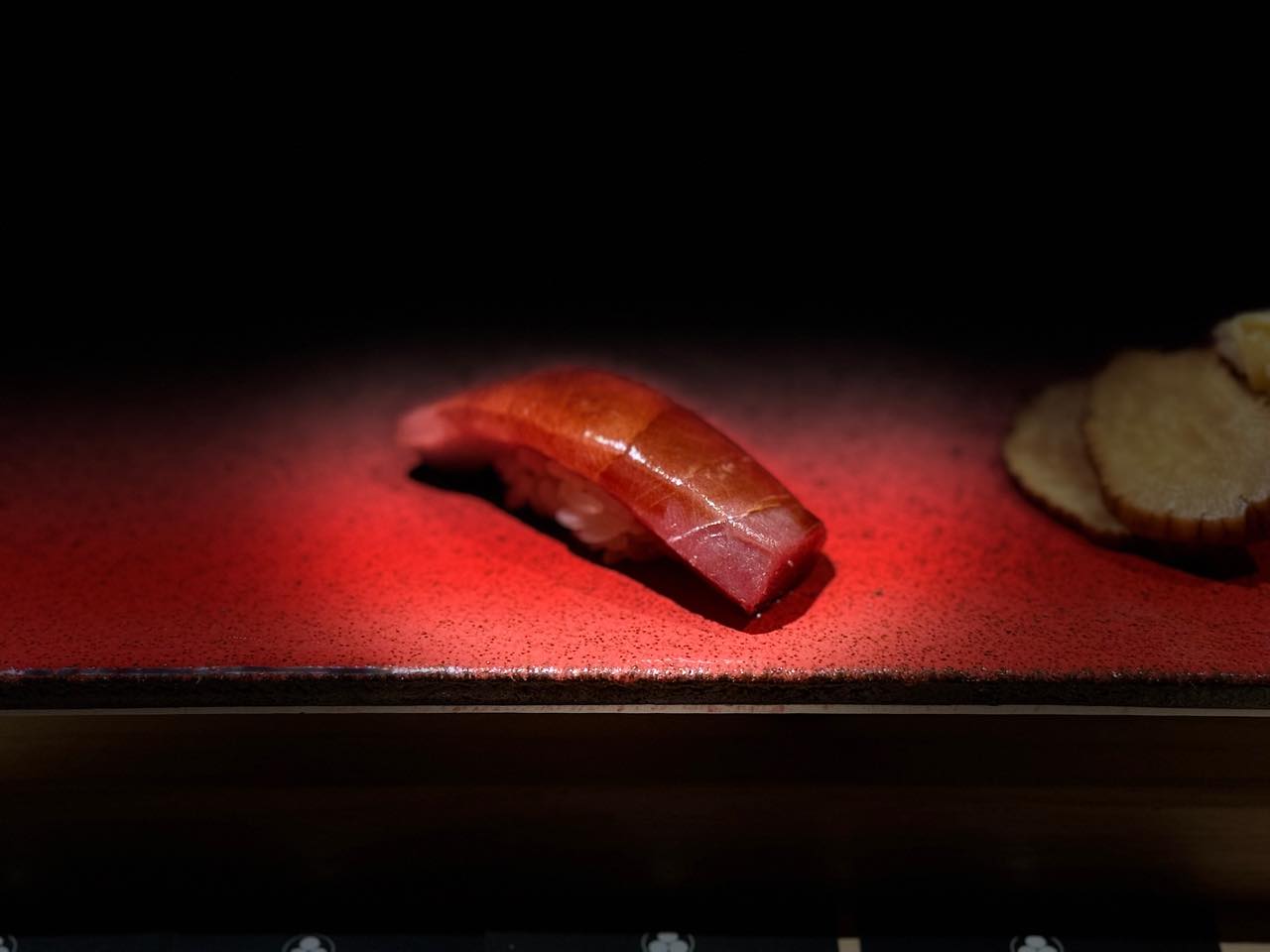 Nigiri akami trên đĩa sơn mài đỏ trong bóng tối