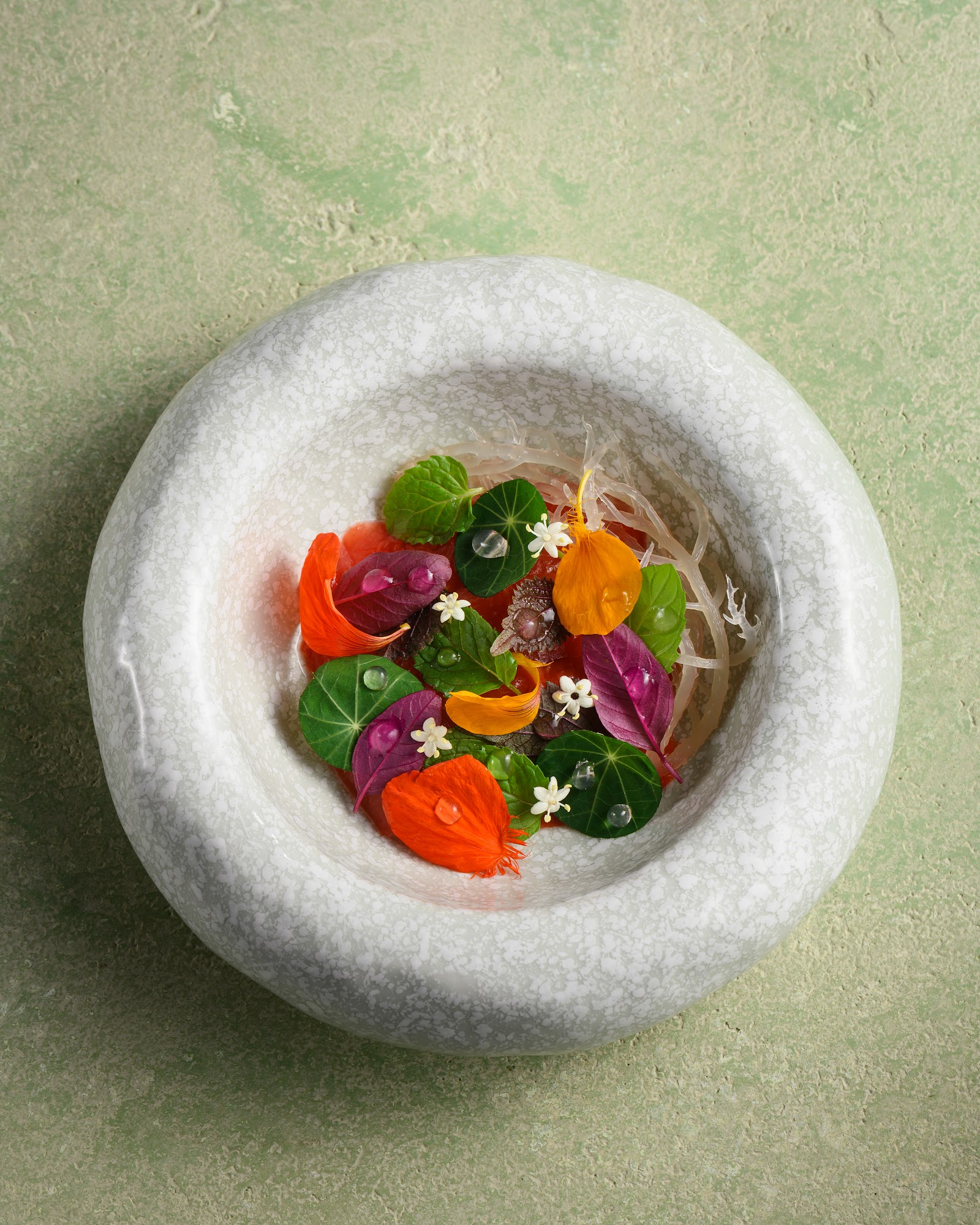 Plant-based tasting course in a white stone bowl with edible flowers
