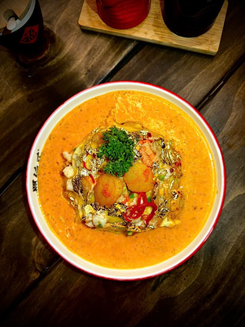 Golden rice bowl from above — glossy broth, shrimp, gold leaf