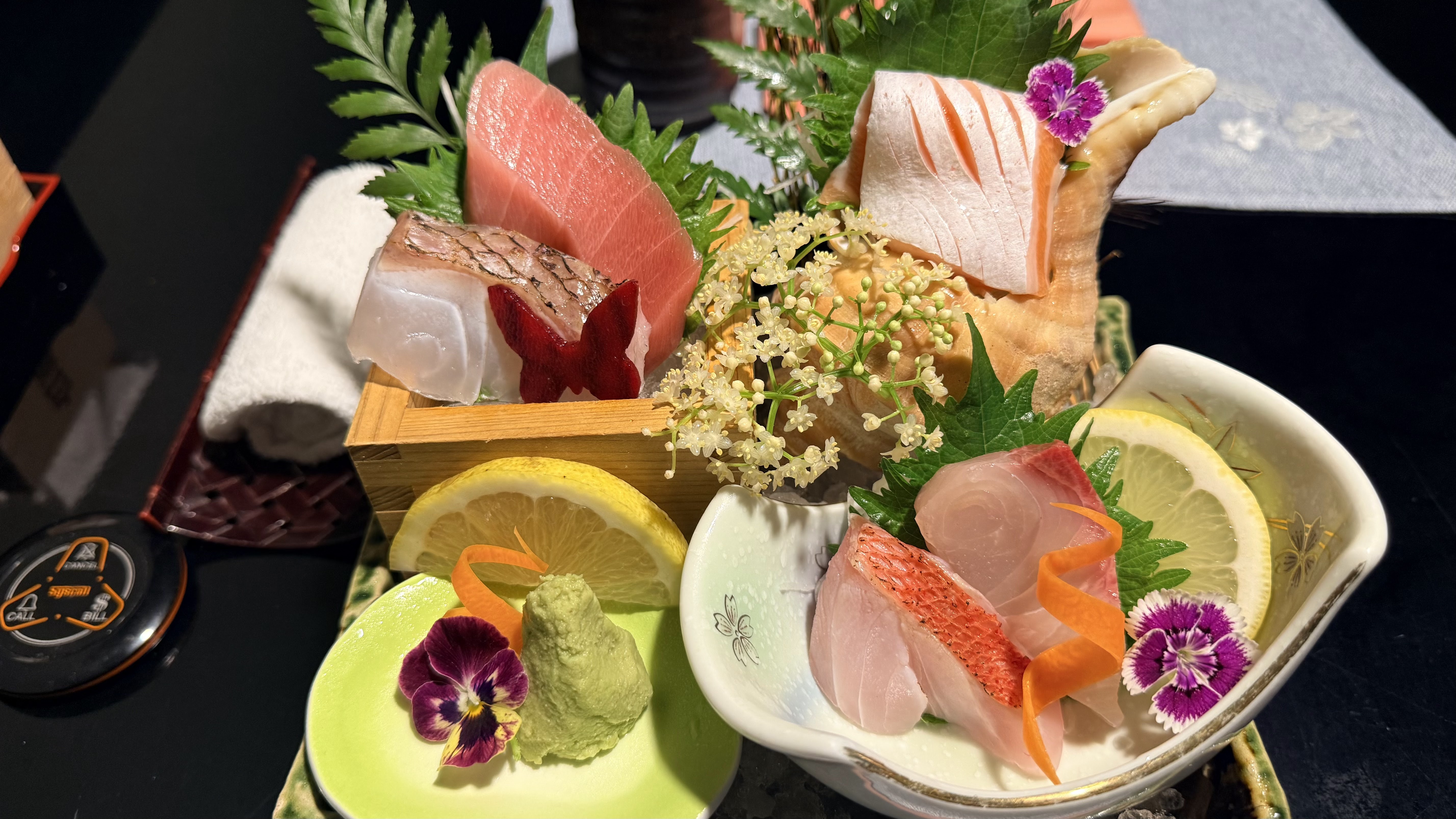Sashimi moriawase close-up — white fish, salmon, wasabi, lemon, edible flowers